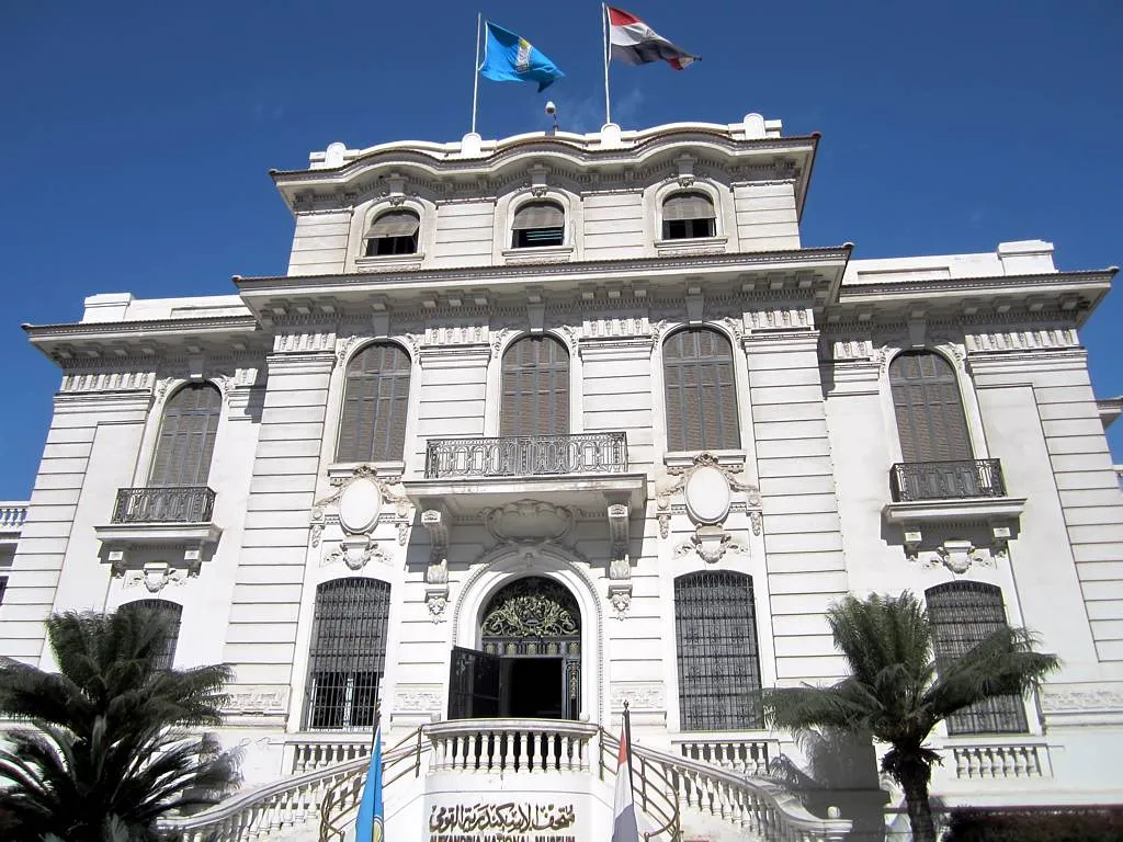 The facade of the Alexandria National Museum, a white colonial-era palace with two flags flying on its roof.