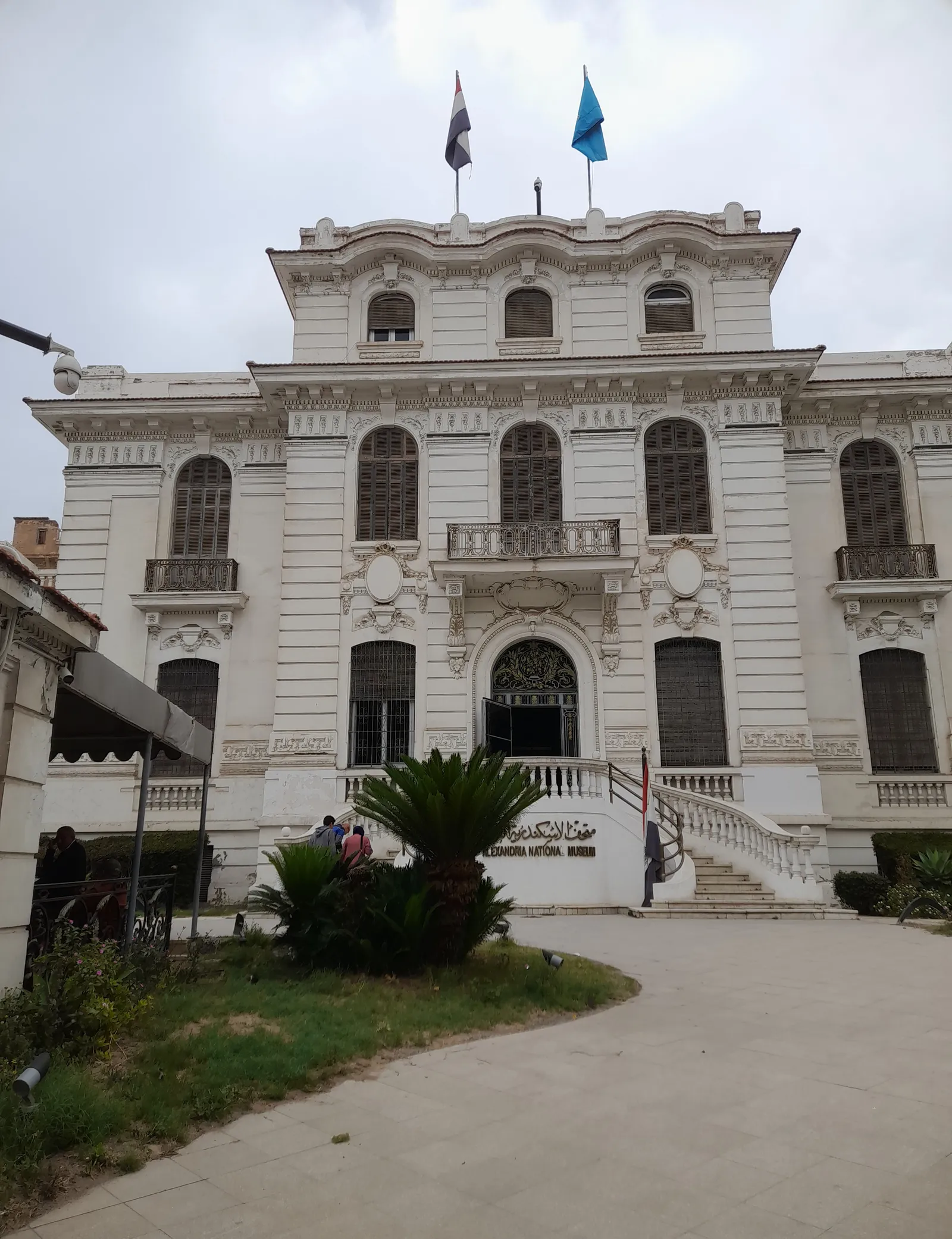 A ground-level view of the Alexandria National Museum's entrance facade with visitors climbing the front steps.