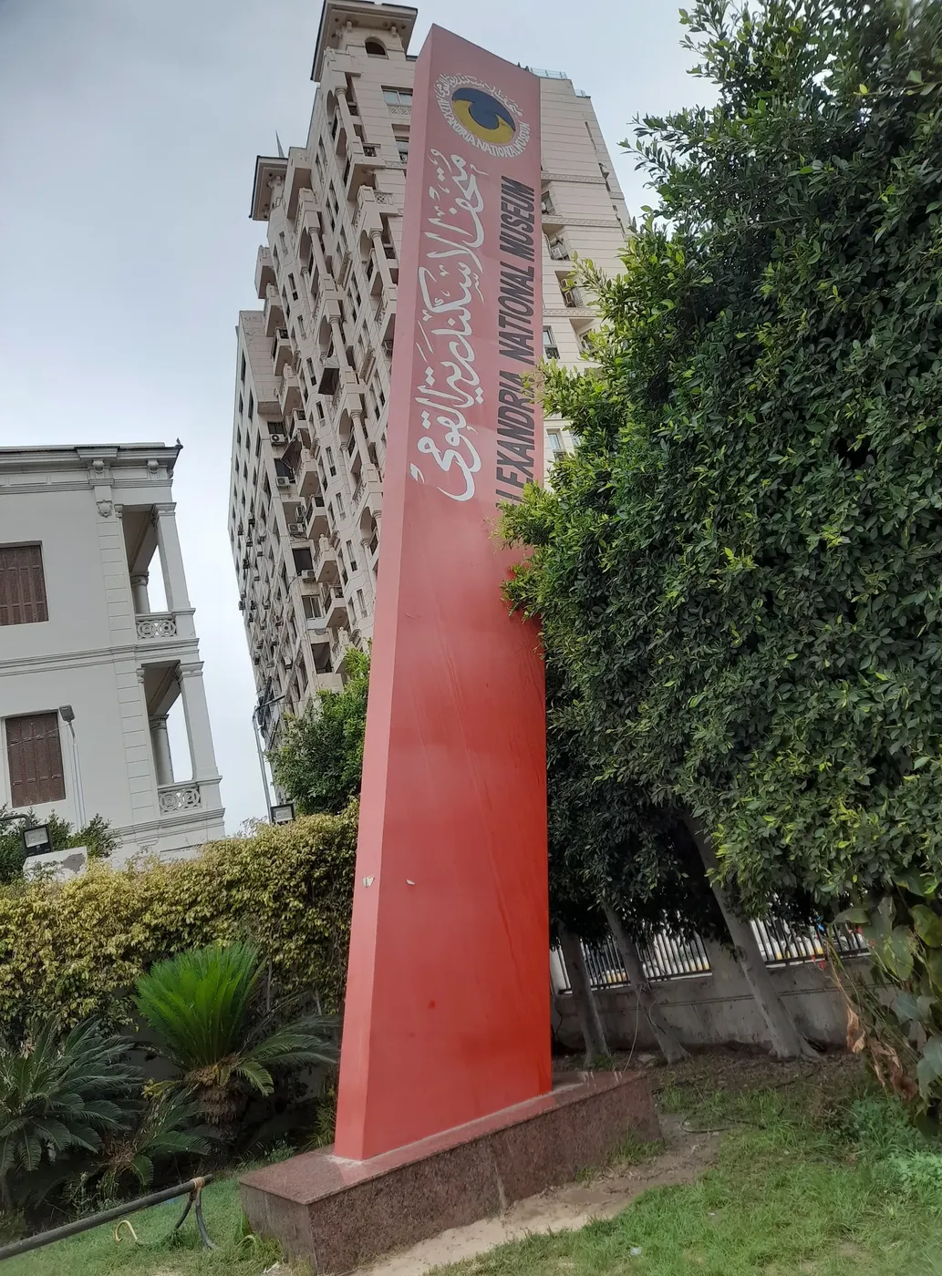 A tall red pylon sign reading Alexandria National Museum in English and Arabic outside the building.