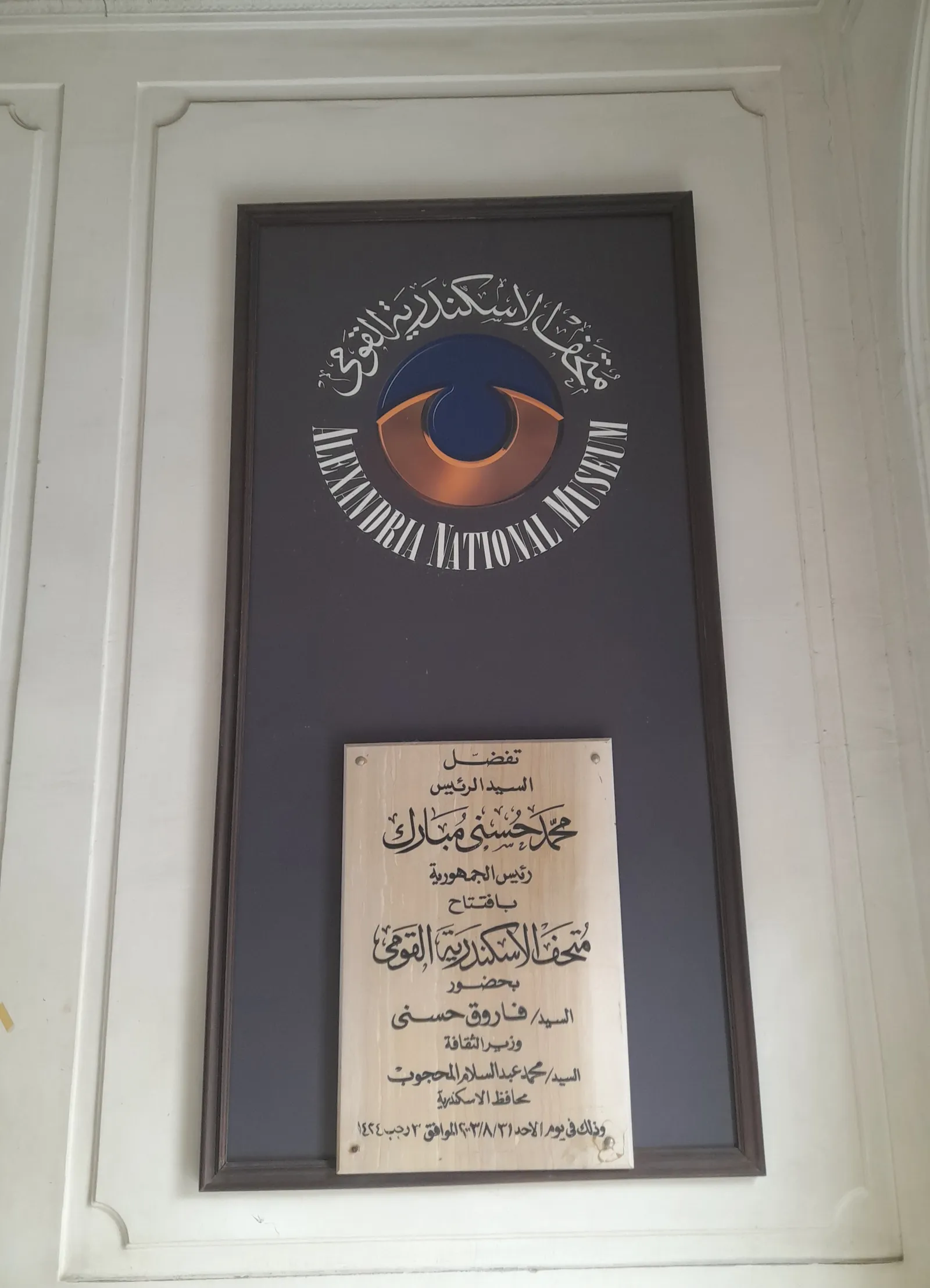 A wall plaque bearing the Alexandria National Museum's circular eye logo above a dedication plaque.