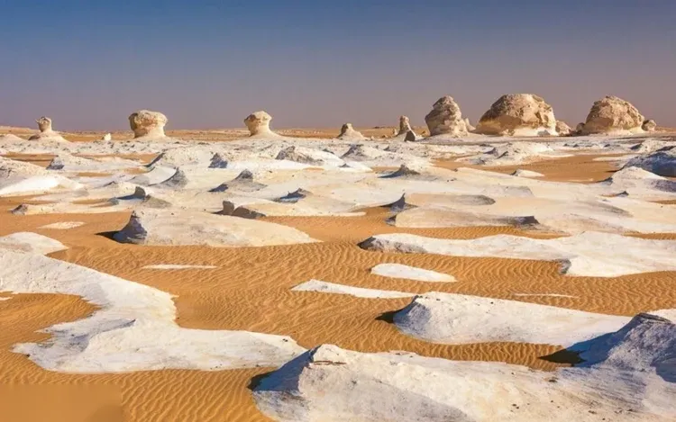 White chalk rock formations rise out of sand dunes streaked with white mineral deposits.