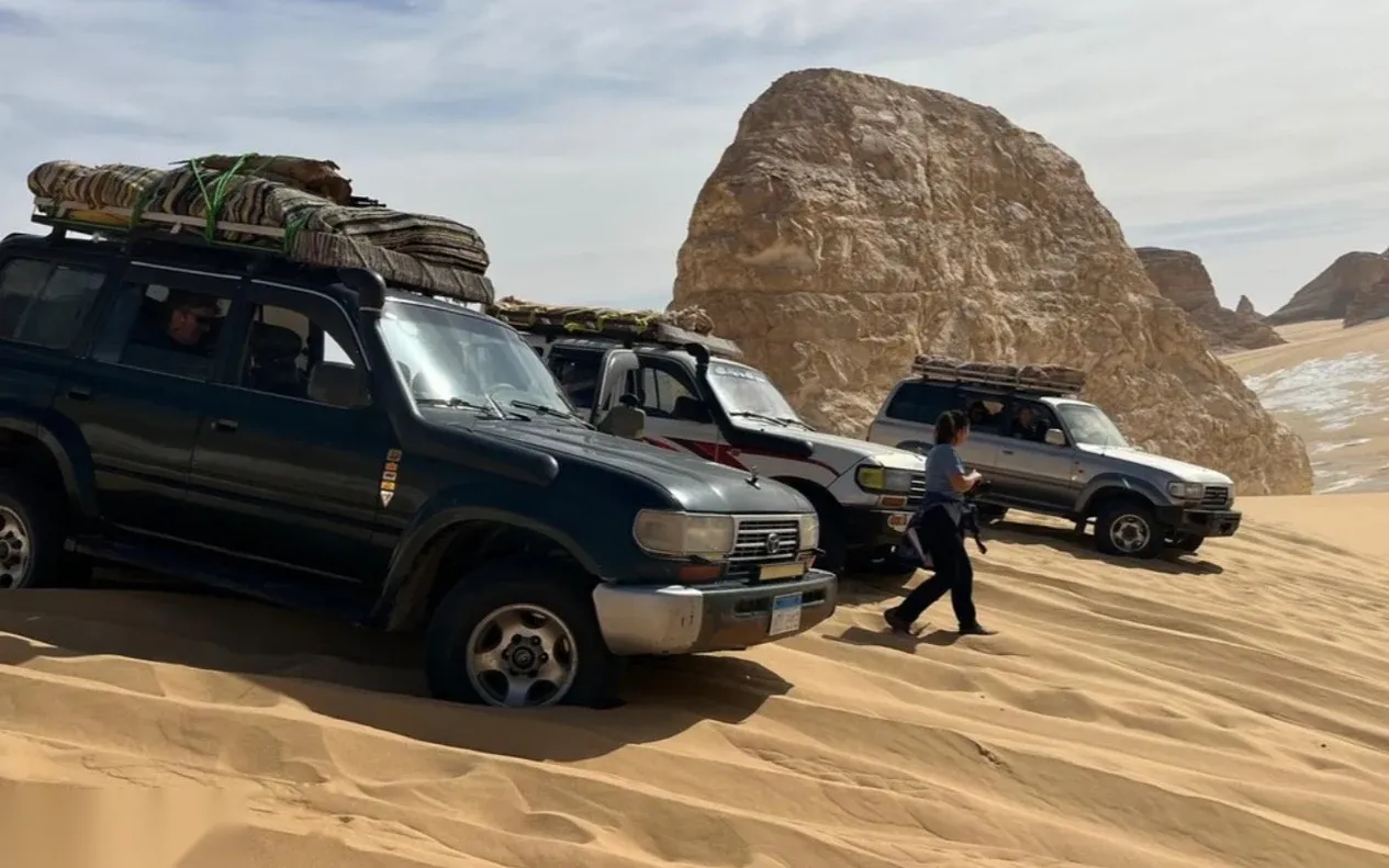 The same three 4x4 Land Cruisers parked beside the large boulder, seen from a slightly different angle.