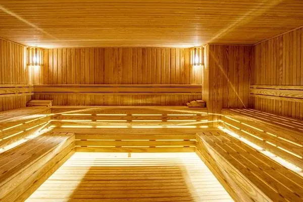 A woman sits on a marble platform covered in bath foam, seen from behind, surrounded by lit candles in a warmly lit hammam bath room.