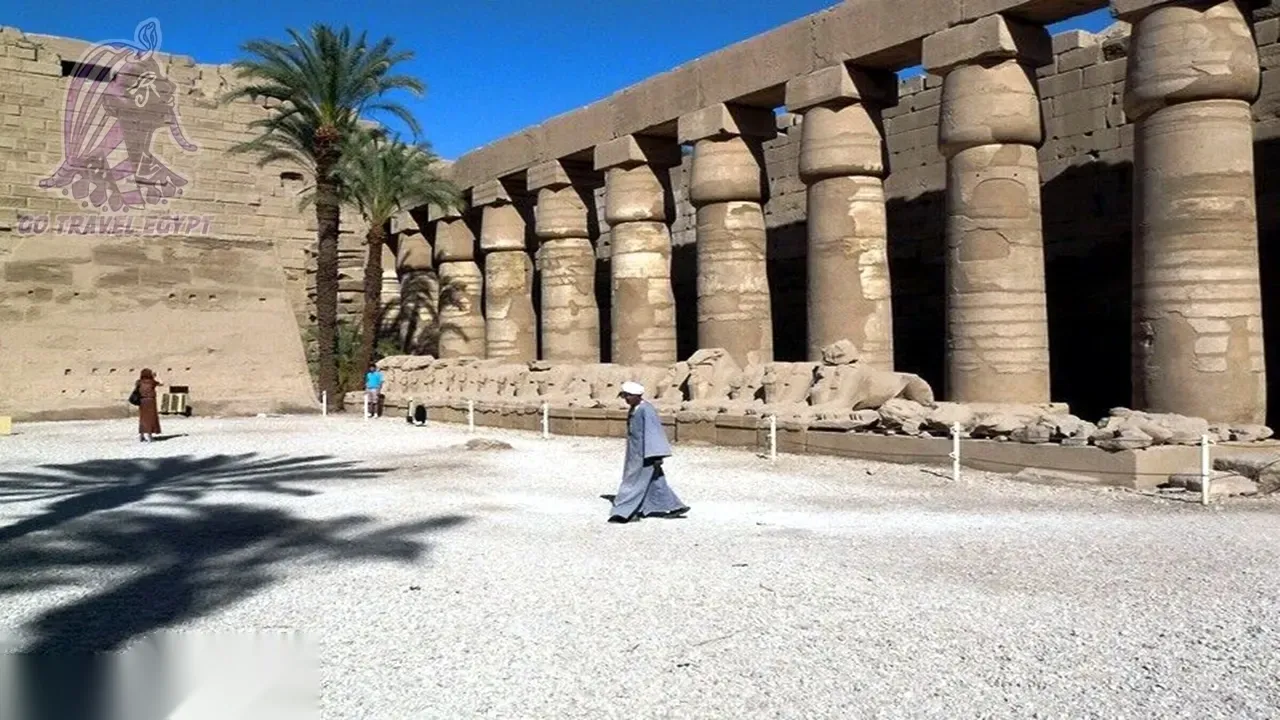 Dendera Temple rises behind a lush green field of crops with a palm tree at dusk.