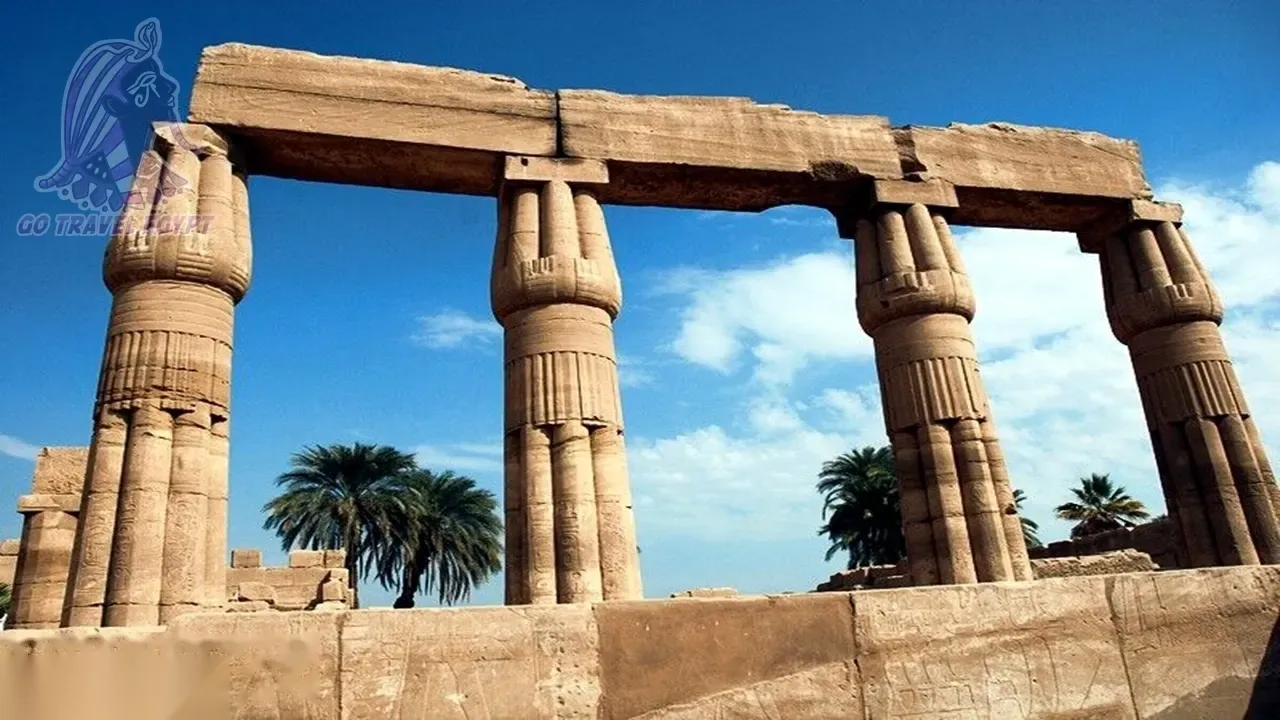 Six tourists pose and wave in front of the ruined stone gateway of a temple entrance.
