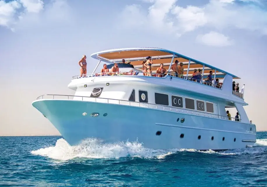 A large white and blue dive boat cruises across open water with passengers gathered on its upper deck.