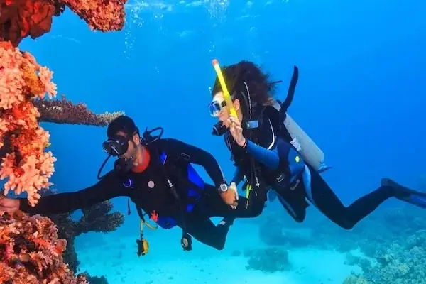 Woman kneeling on a dive boat deck administering oxygen to a diver lying down, oxygen kit beside her.