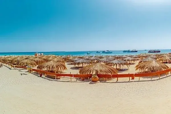Panoramic view of straw beach umbrellas lined along the shoreline with tour boats anchored offshore.
