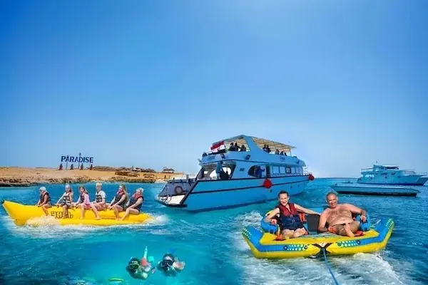 Composite scene showing a family banana boat ride, a docked tour boat, a towable inflatable ring, and snorkelers near a 'Paradise' island sign.