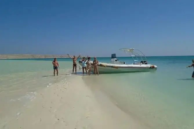 White glass-bottom boat anchored in shallow turquoise water with an empty upper deck and coastline in the distance.