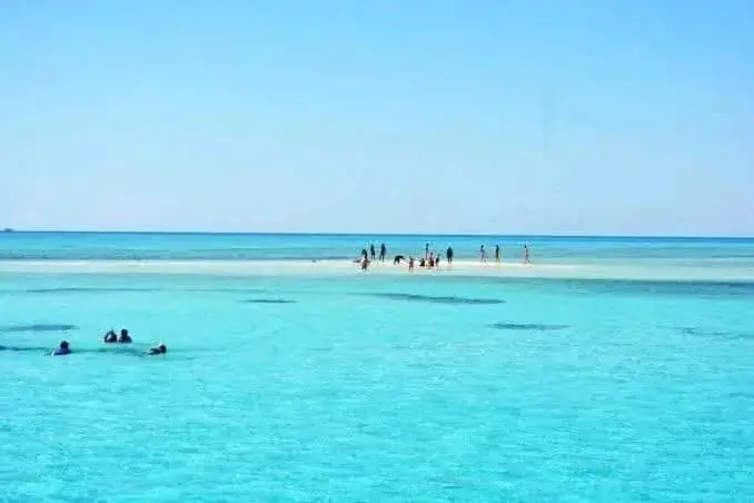 White and dark-blue glass-bottom boat with an open upper deck anchored in bright turquoise water.