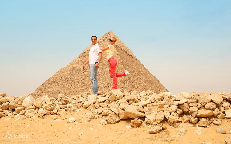 Three riders sit on red quad bikes posing for a photo with several Giza pyramids lined up in the background.