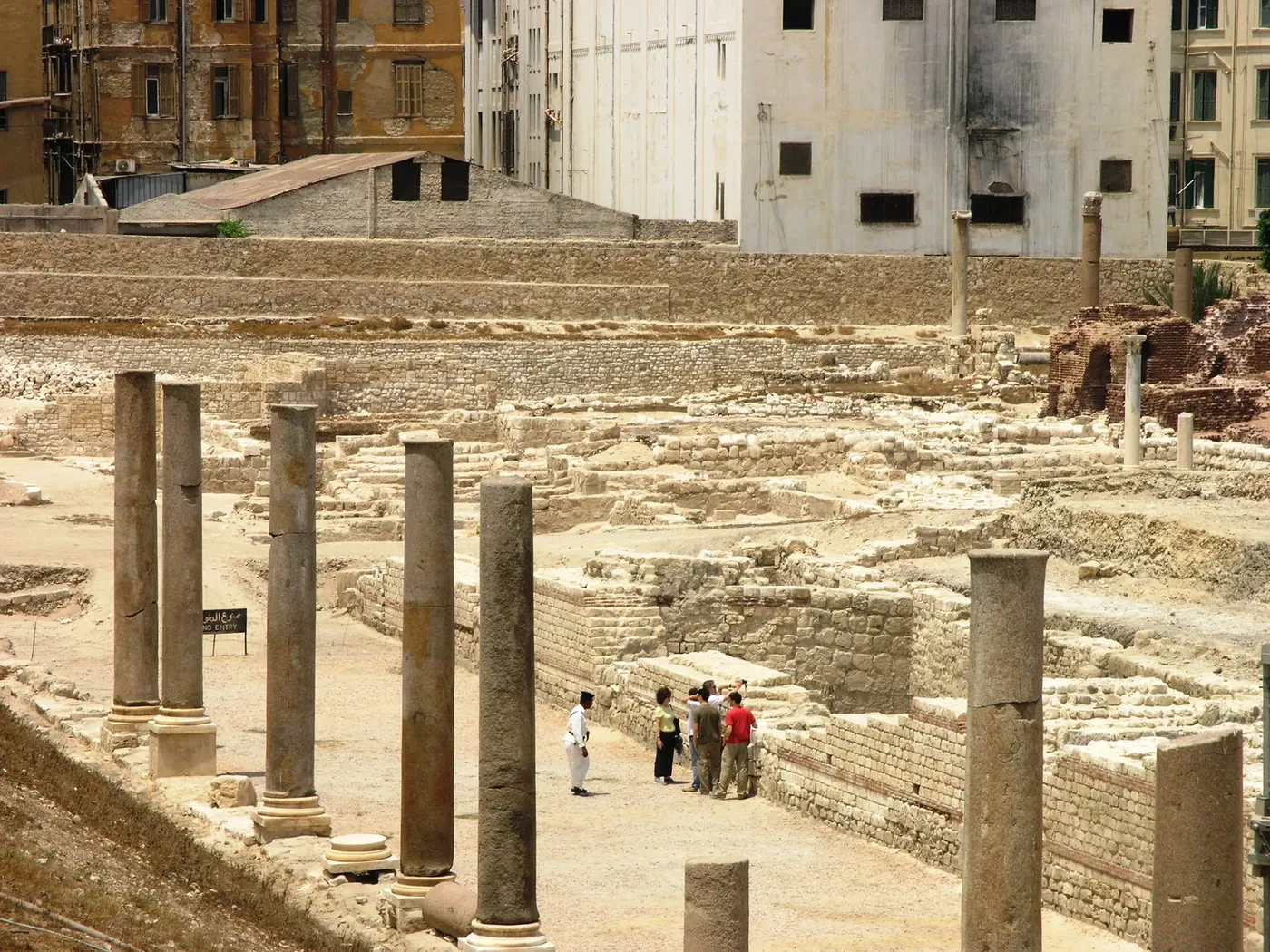 Semi-circular stone seating of the Roman amphitheater in Alexandria, with marble columns and green trees in the background.