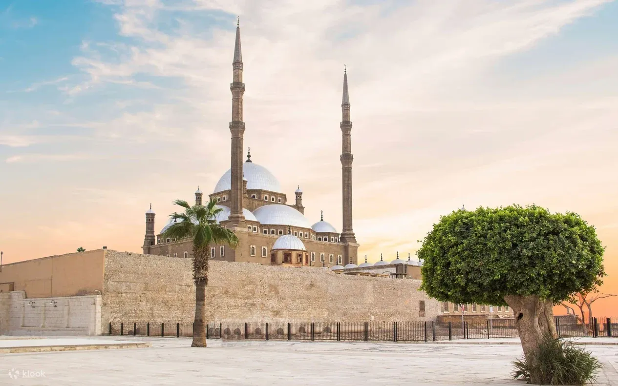 An aerial view of the domed and minaret-topped mosques of the Citadel rising above the dense Cairo skyline.