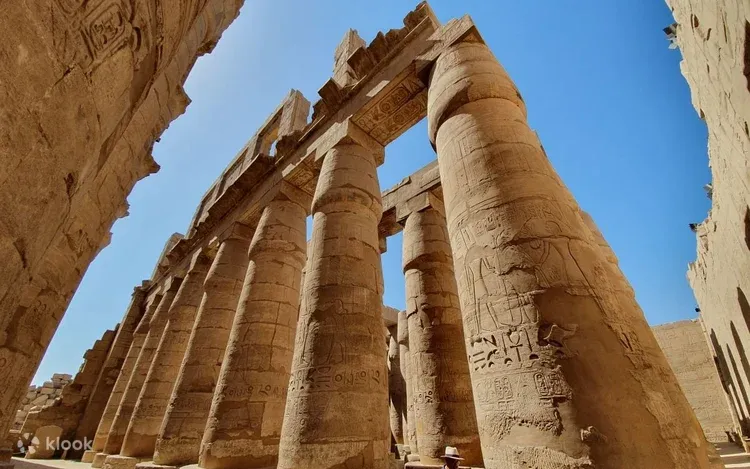 Two giant stone statues of a seated pharaoh wearing the double crown flank a crowded temple walkway at Karnak.