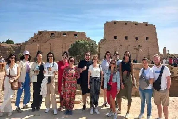 A group of about thirteen tourists poses together in front of the ruined pylon walls of Karnak Temple.