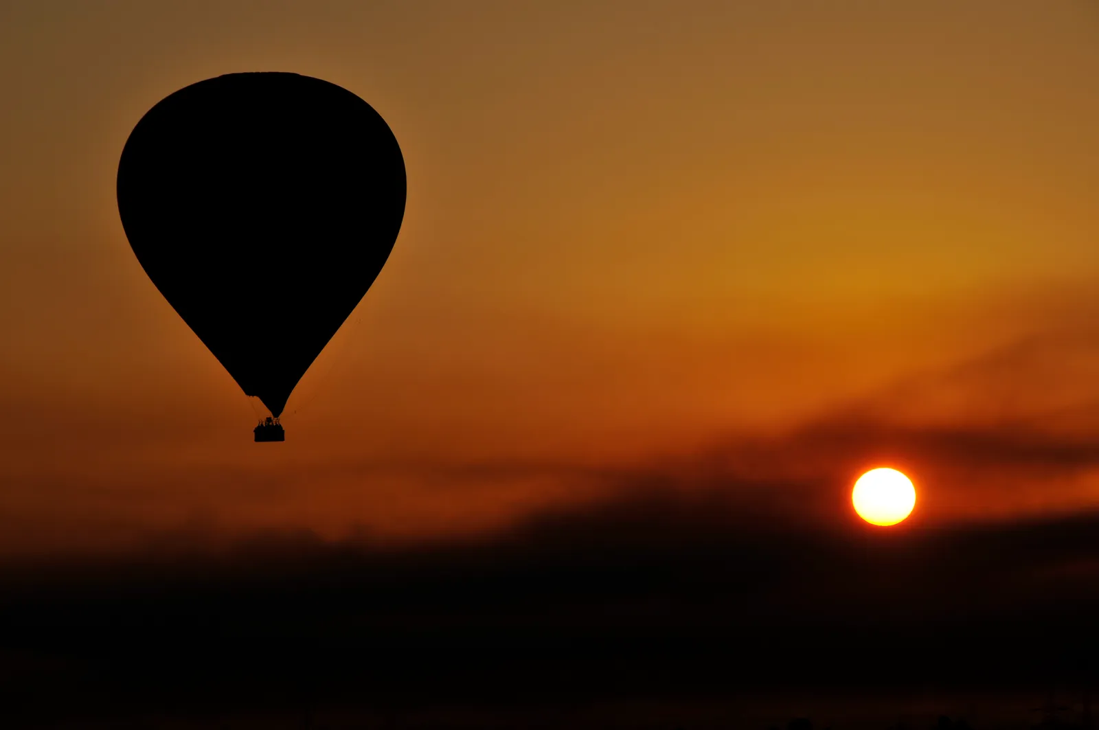 Multiple hot air balloons lift off and hover low over a launch field at dawn, seen from inside another balloon's basket.