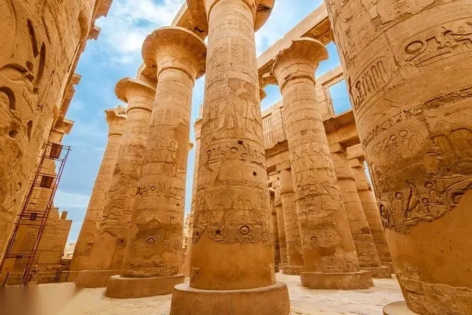 A group of travelers poses on the ramp leading up to the Temple of Hatshepsut, its rows of columns cut into the cliffs behind them.