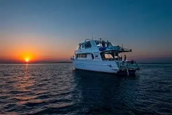 A private motor yacht at sunset, silhouetted against an orange horizon on calm water.