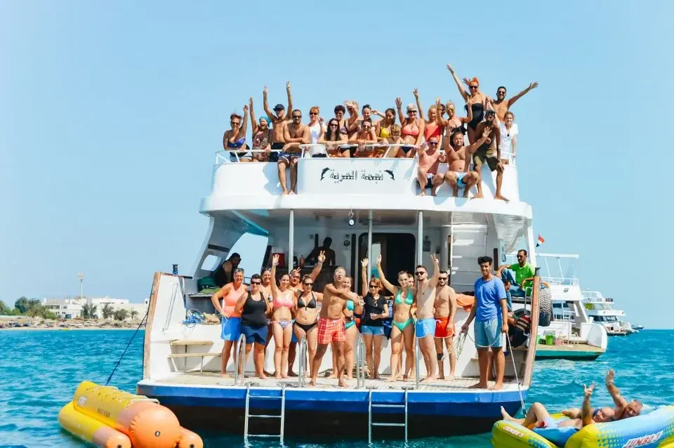 A luxury motor yacht with sunbathing passengers on cushioned seating cruises past a busy marina.