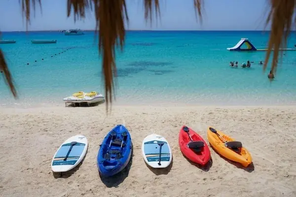 A couple sits together on a narrow strip of white sand surrounded by shallow turquoise water, viewed from behind.