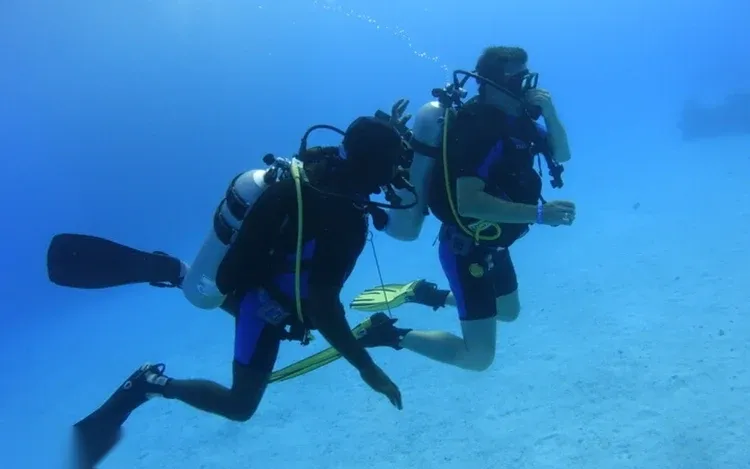A snorkeler swims just above a green sea turtle gliding through clear turquoise water.
