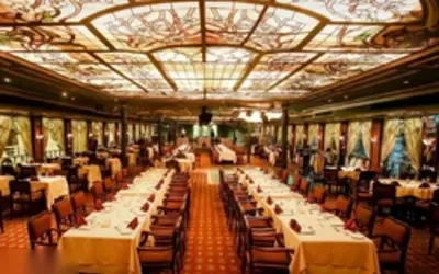 The ornately decorated main dining hall of a Nile cruise boat, with a stained-glass ceiling and rows of set tables.