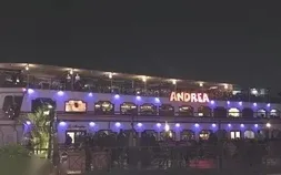A similar aerial view of the same bow dining area, with guests eating and river lights reflecting on the water.