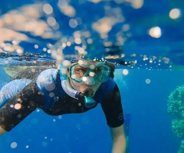 Two divers standing in shallow water, one carrying a tank labeled NITROX, chatting and smiling at each other.