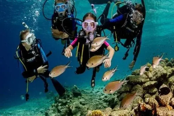 Instructor and two students kneeling on a sandy seabed during an underwater skills session.