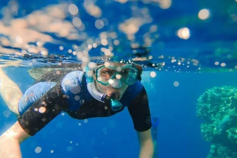 Instructor kneeling on a sandy seabed giving briefing hand signals to three student divers gathered around him underwater.