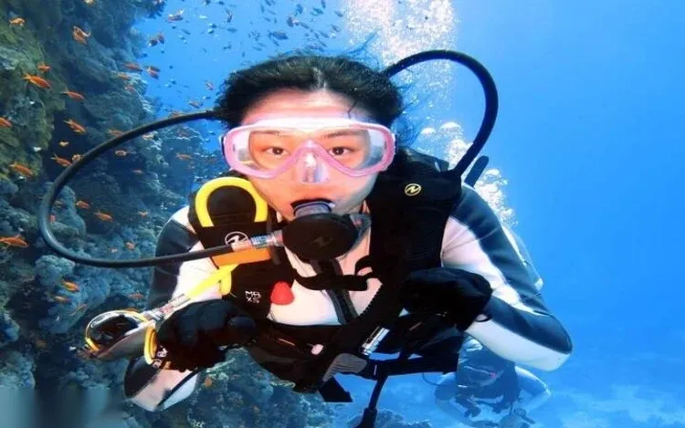 Close-up portrait of a diver in a pink mask hovering beside a coral reef with orange anthias fish.
