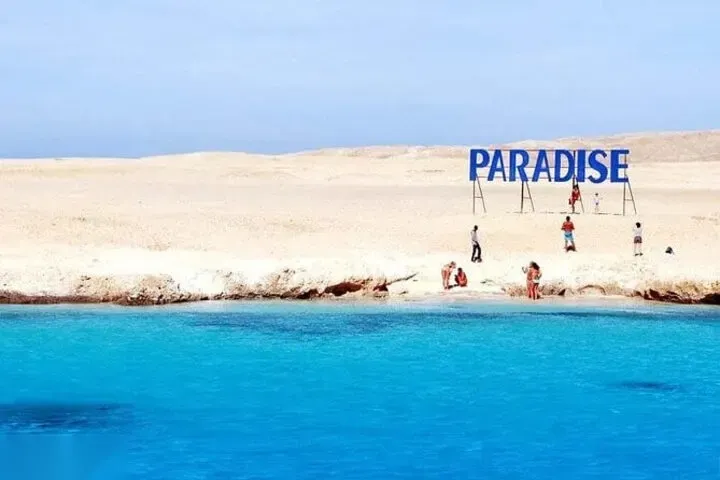 Several tour boats and a sailboat are anchored over a shallow turquoise reef.