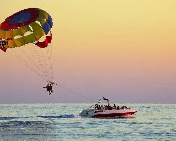 A father and young son ride tandem in a parasailing harness, both barefoot and smiling.