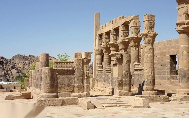 Carved sandstone columns with Hathor-head capitals stand among the ruins of Philae Temple.