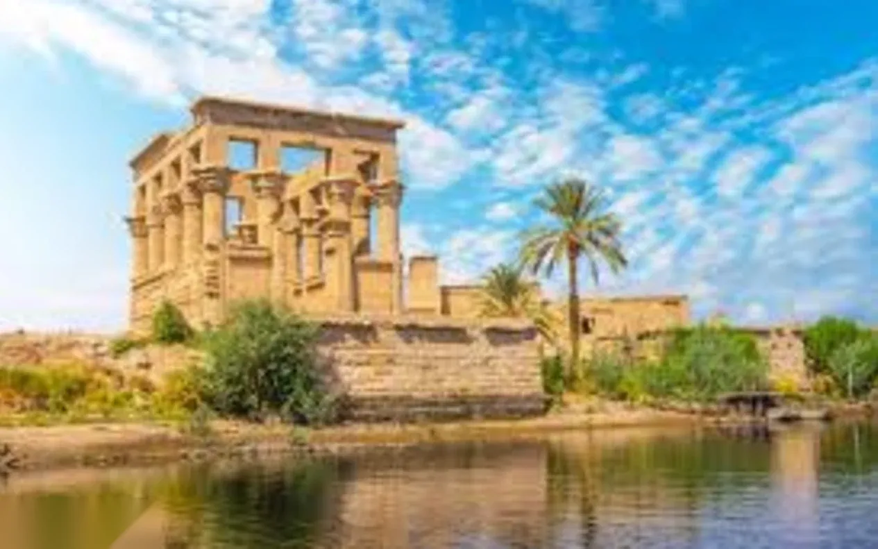 Philae Temple's Kiosk of Trajan is reflected in the Nile, with a palm tree beside its ancient stone columns.