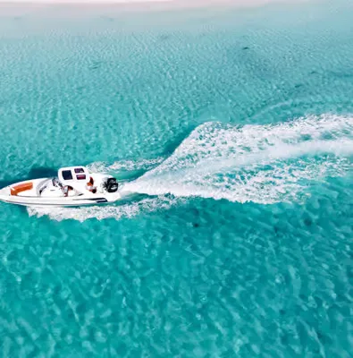 Aerial view of the white motor yacht anchored in bright turquoise water with two crew members standing on deck.