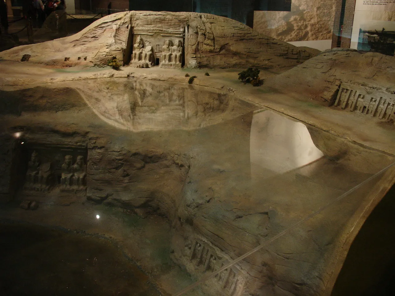A small group of tourists walks along a path toward the seated colossal statues at the entrance of the Great Temple of Abu Simbel.