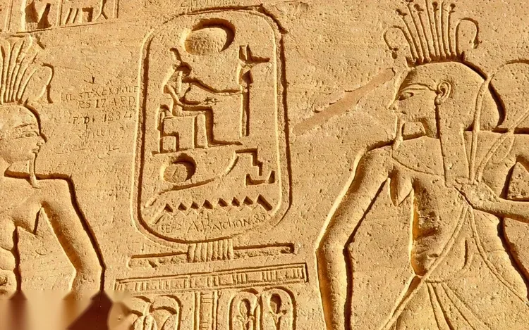 Close-up of a carved hieroglyphic cartouche and figures on a sandstone wall at Abu Simbel, worn by time.