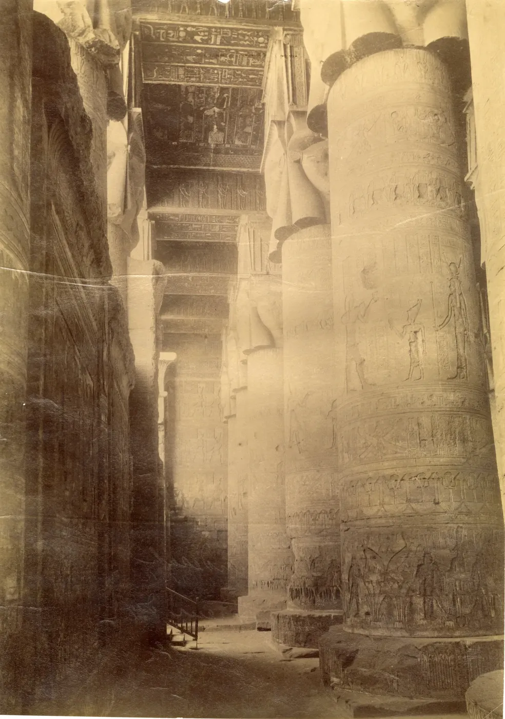 Exterior corner view of the Temple of Hathor at Dendera showing its massive facade and Hathor-head columns against a partly cloudy sky.