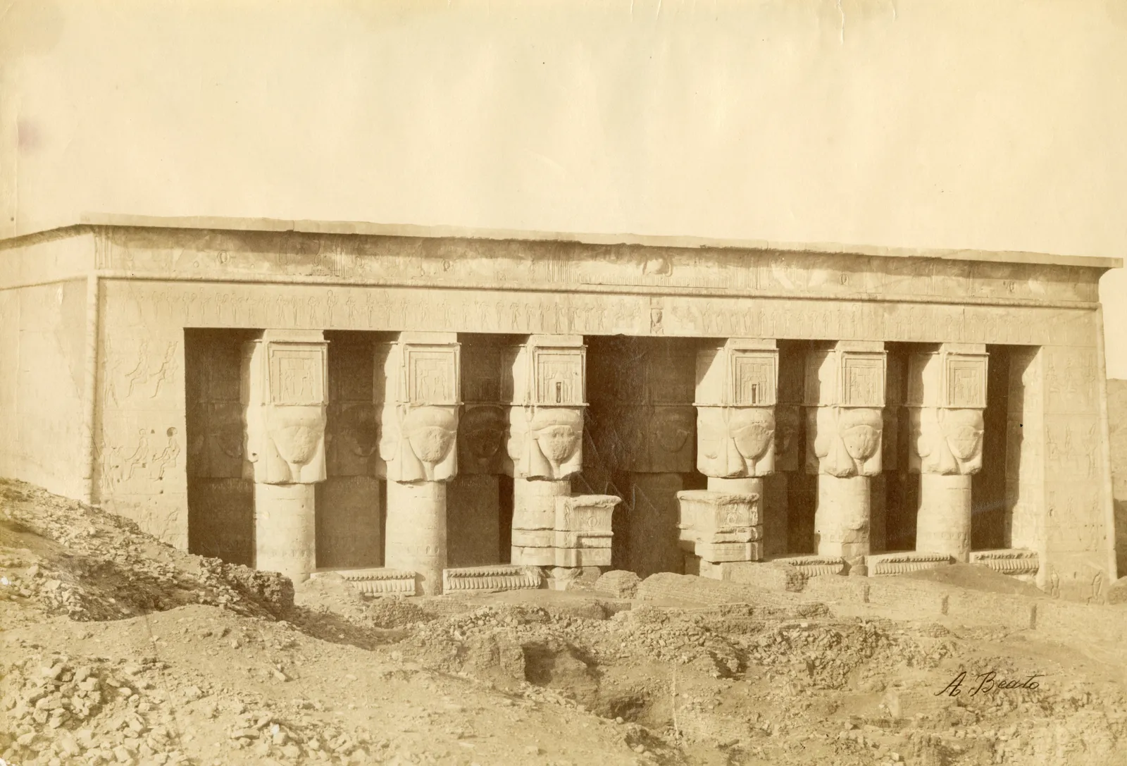 Tour guide speaking to a group of visitors in front of the Dendera Temple entrance with palm trees on either side.