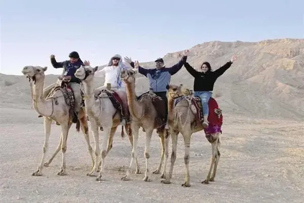 Two people on horseback leading a third horse across open sandy desert with mountains in the background.