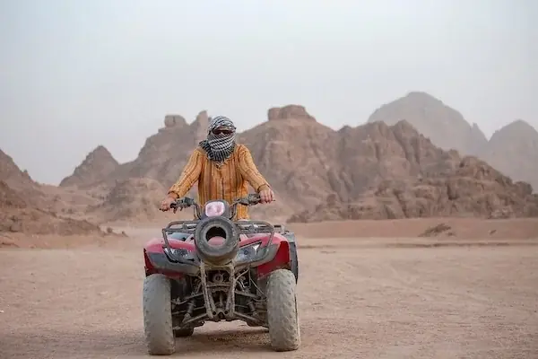 Woman riding a galloping white horse across rocky desert terrain at sunset.