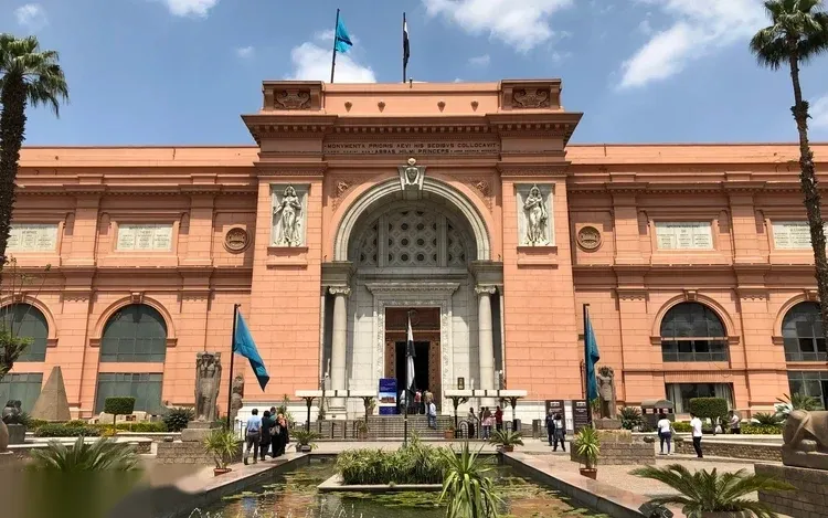 The pink neoclassical facade of the Egyptian Museum in Tahrir Square, with flags and a reflecting pool out front.