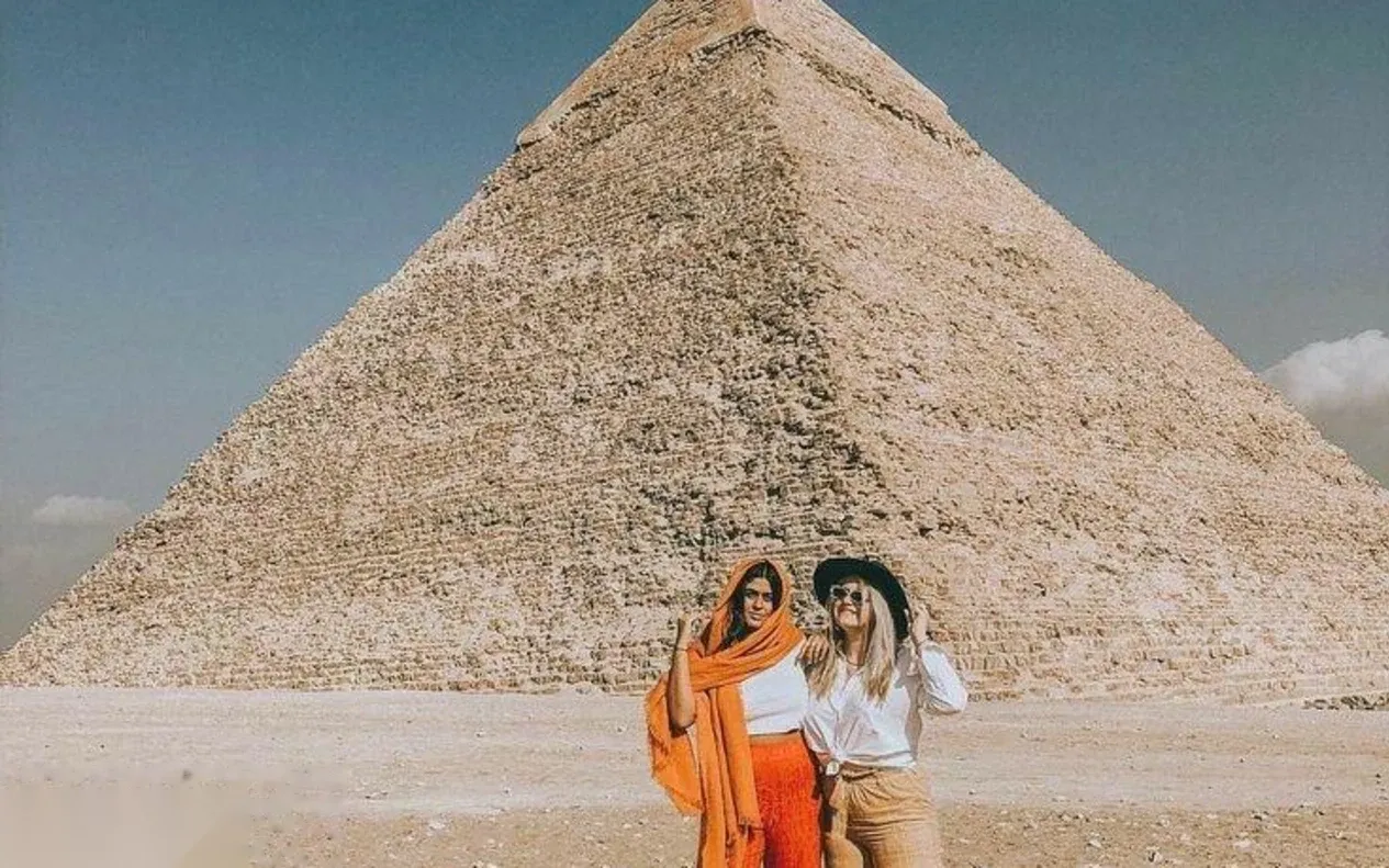 Two women posing arm in arm in front of a Giza pyramid on a sunny day.