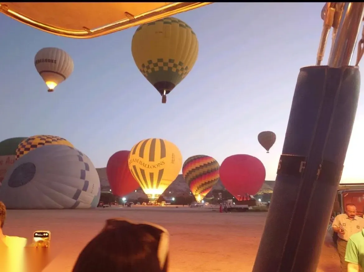 Several hot air balloons inflating on the launch field before dawn, glowing orange from their burners.