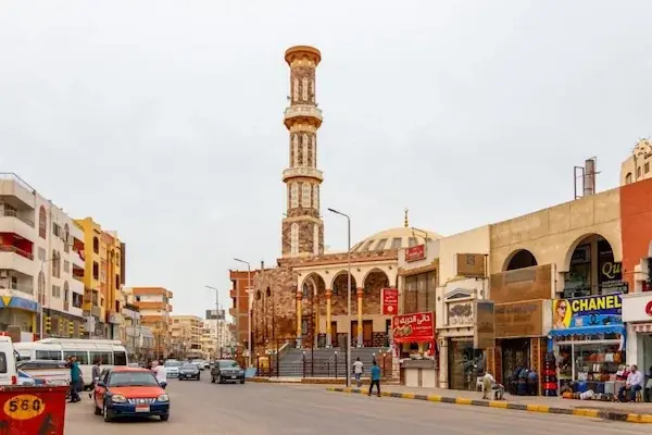 A street in downtown Hurghada with the tall minaret of El Mina Mosque rising above traffic and shopfronts.