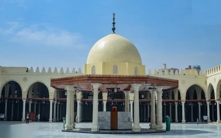 A domed stone ablution kiosk in the courtyard of a historic Cairo mosque, surrounded by horseshoe-arch arcades.