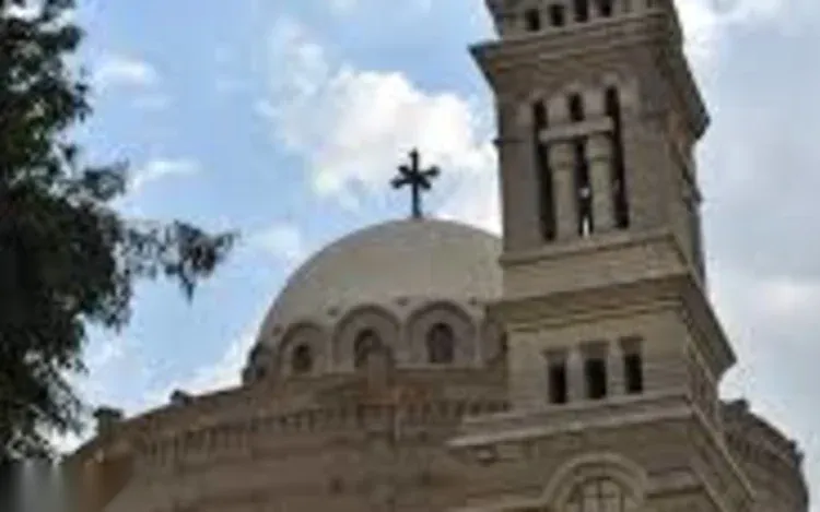 The bell tower and dome of a Coptic church topped with a cross, seen against a partly cloudy sky.