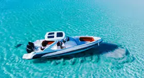 Aerial view of a white speedboat drifting over shallow turquoise water near a sandbar.